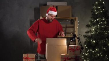 Noel Baba kostümü giymiş sakallı beyaz bir adam büyük bir kutudan kırmızı kurdeleli küçük olanları indiriyor. Tatil için büyük indirim konsepti.