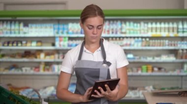 Portrait of a busy female sales assistant in a grocery typing on the digital tablet while taking inventory. Selective focus