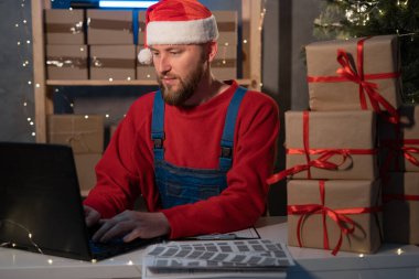 Small business aspiring entrepreneur, SME freelance worker working in a home office man in Santa Claus hat and accepts an online order using an application and a laptop, Christmas sale concept
