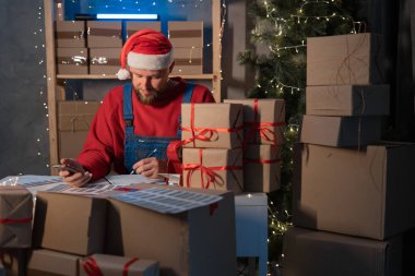 Küçük işletme sahibi teslimat servisi ve Noel 'de paketleme kutusu, iş sahibi Noel Baba posta ofisine müşteri göndermeden önce kontrol emri için çalışıyor, Sevkiyat Çevrimiçi Satış.