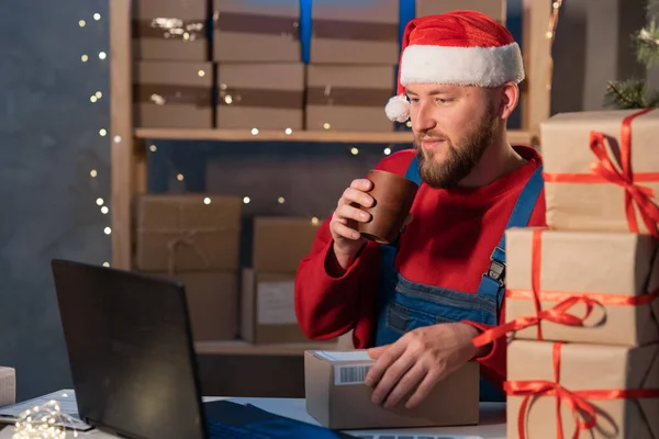 Santa Claus start up small business entrepreneur SME freelance man typing computer drinking coffee with box, online marketing packing box and delivery, Christmas sale, SME warehouse e-commerce concept