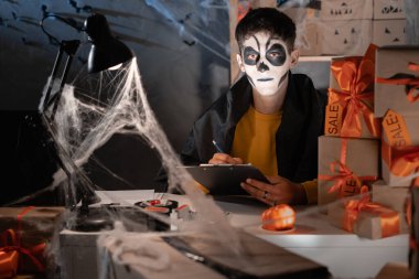 Teslimat işi ve teslimat işi. Kafatası makyajlı bir adam evdeki ofiste örümcek ağı kutularının arasında oturur ve gönderilecek kutuları takip eder. Cadılar bayramı, indirimler ve promosyonlar için büyük indirim kavramı.