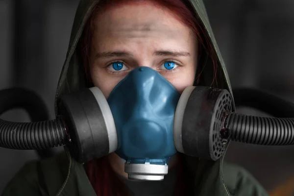 Post apocalypse female survivor. Young pandemic survivalist woman in gas mask looking in front of her on the background with apocalyptic war area around. Sad woman in breathing oxy mask. Close up