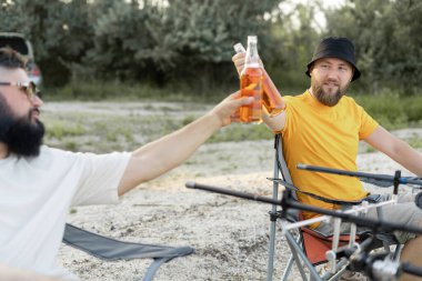 Erkek arkadaşlar gölde balık tutuyor ve bira içiyor. eğlence ve insan konsepti
