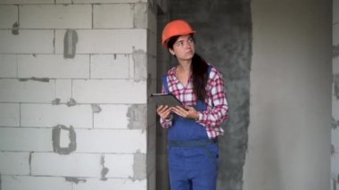 İnşaat halinde aletli bir mühendis. İnşaat alanındaki miğferli kadın mühendis veya mimar endüstriyel elektronik tabletle çalışıyor.