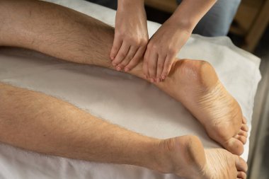 Spor fizyoterapisi konsepti için klinikteki hasta sporcuya bacak ve baldır masajı yapan kadın terapisti kapatın.