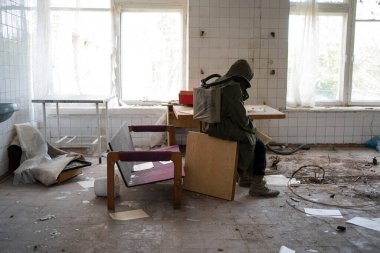 Gaz maskeli, yıkık dökük bir binada oturan kıyamet sonrası hayatta kalanlar. Çevre felaketi. Çevre kirliliği, ekolojik felaket, nükleer savaş, kıyamet sonrası kavramı.