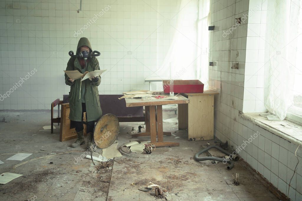 Female disaster survivor in a post apocalyptic setting wearing a gas mask and reading a document. Environmental pollution, ecological disaster, nuclear war, post apocalypse concept.