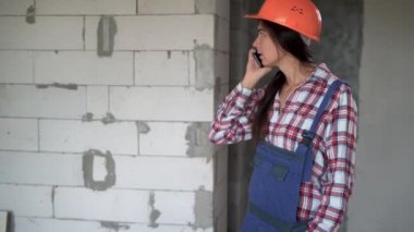 İnşaat ofisindeki akıllı telefondan kasklı kadın müteahhit arıyor. mimari, inşaat işi ve inşaat kavramı