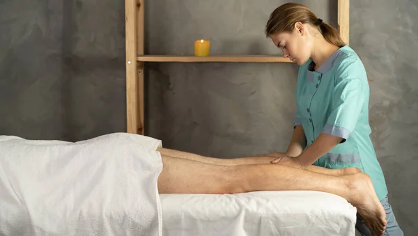 Female therapist giving leg massage to athlete patient on the bed in clinic or spa. sports physical therapy concept