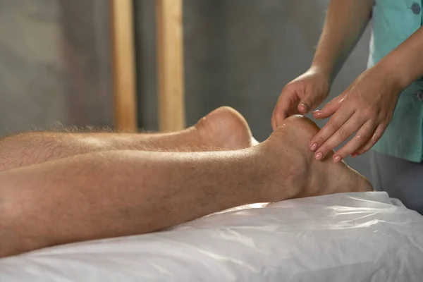 按摩师在温泉沙龙的桌子上按摩男性腿脚的手的特写 运动和治疗性按摩概念 — 图库照片