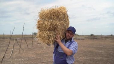 Saman balyalı çiftçi, organik tarım için saman çöpü taşıyan adam. Tarım çiftliği ve kurumuş saman çöpü yığını..