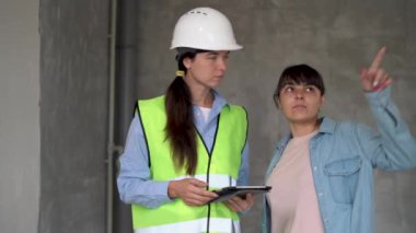 Satış temsilcisi yeni binada müşteriyle konuşuyor. İnşaat alanında müşteriyle emlakçılık yapan bir kadın. Gayrimenkul komisyoncusu evini genç bir kadına gösteriyor..
