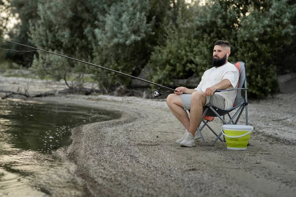 Γενειοφόρος Άνδρας Που Ψαρεύει Στη Λίμνη Κάθεται Στην Προβλήτα Κοντά — Φωτογραφία Αρχείου