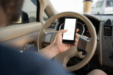 Ekranda beyaz model akıllı telefonu olan erkek el kamerasının yakın çekimi, direksiyonun arka planı, GPS navigatör uygulaması ile konumu aranıyor. Boşluğu kopyala