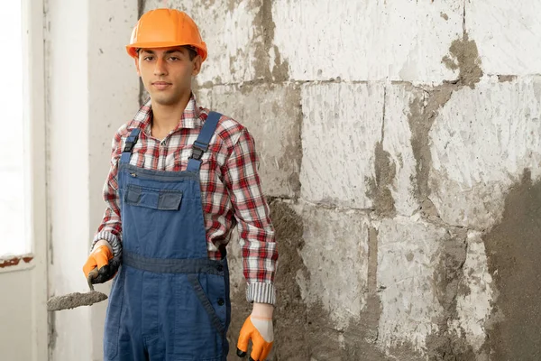 Arabic man master plasters the walls, portrait of builder in hard hat making repairs in the apartment, the concept of repairing and remodeling the house