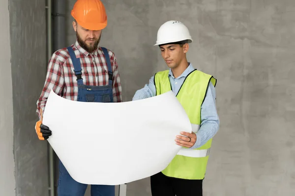 建築家や建設エンジニアや測量の議論の計画や設計図 2人の男が硬い帽子をかぶっていて 屋内の家の建設現場に立っている スペースのコピー — ストック写真