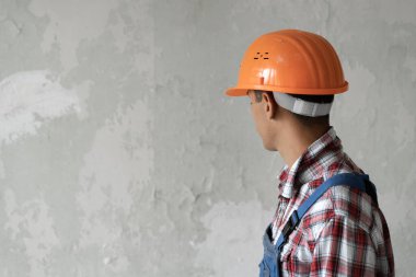 Fotokopi alanı olan kendine güvenen yakışıklı erkek inşaat işçisi gri arka planda kalıp duvarın kenarına bakıyor.