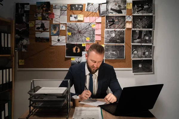 detective man working with evidence at desk in office, evidence board in the background, copy space
