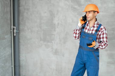 Güvenlik kasklı profesyonel Arap inşaatçı duvar arkasında bir telefon görüşmesi, ev yenileme ve iletişim konsepti