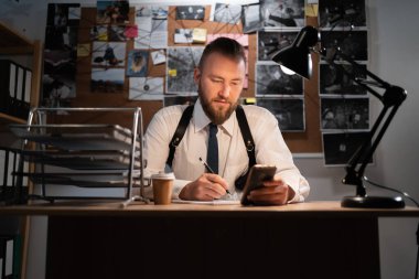 Dedektif ofisteki kanıt panosuna bakıyor.