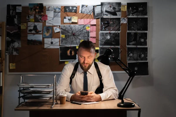 Detective working at desk in his office using mobile phone for searching information, copy space