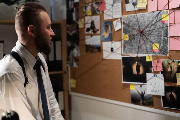 Detective looking at evidence board in office, working at night, copy space