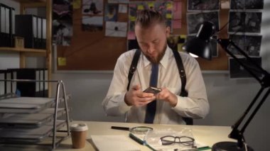 Ofiste elinde kanıtlarla çalışan bir dedektif, bir suç davasında delillerin fotoğrafını çeken bir cep telefonu kullanıyor.