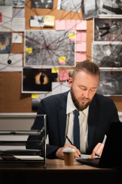 Masada oturan ve deftere yazı yazan profesyonel dedektif, suç araştırmacısı, dava detaylarını yazan, suç mahallinden toplanan polis dedektifi belgeleri.