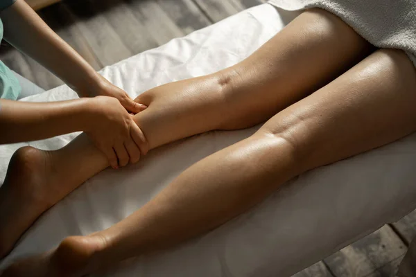 Masseur making legs massage in spa salon, close up view. Massage therapist working with patient, massaging his calves.