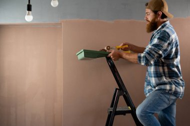 Ressam, turuncu arka plandaki merdivene bir duvar boyuyor. onarım, inşa ve ev konsepti