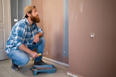 Şüpheci boyacı duvarın yanında tekerlekli sandalyeyle otururken düşünür. DIY konseptinde evi boyayan adam
