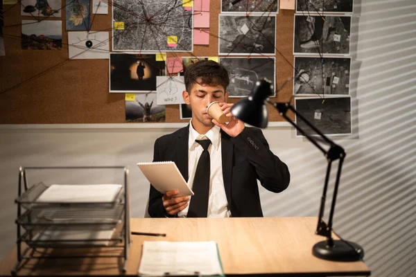 Detective working at desk in his office, drinking coffee and thinking of searching for solution, copy space
