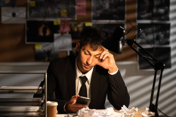 Worried frustrated detective in dark suit sitting at an office desk full with papers being overloaded with work. Stressed investigator in police department. business, stress, emotions and fail concept