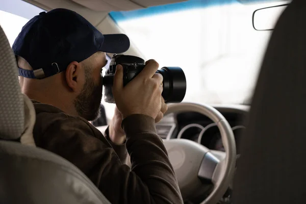 Private detective sitting inside car doing surveillance work photographing with camera, inside view