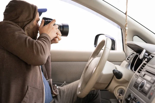 Private detective sitting inside a car photographing with a professional camera