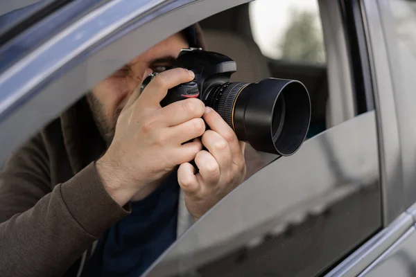 Investigator or private detective, reporter or paparazzi sitting in car and taking photo with professional camera, close up