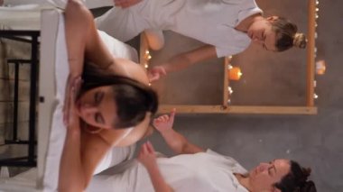 İki masöz dört elle masaj yapıyor. Müşterinin kalçalarına ve bacaklarına masaj yapan masörler. Genç bir kadın kaplıca salonunda çifte yağ masajı yaptırıyor. Dikey video