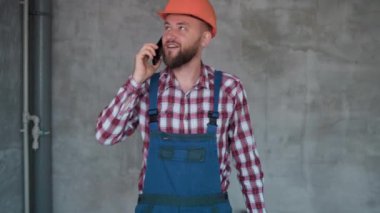 Mutlu gülümseyen sakallı işçi ya da inşaatçı duvar arkası olan akıllı telefondan arıyor. meslek, inşaat ve onarım kavramı