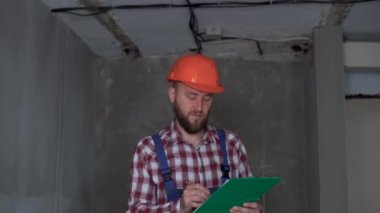 Yeni evde panosu olan işçi tulumlu bir erkek sanayi mühendisi. Güvenlik ekipmanları. Sakallı yakışıklı erkek müteahhit. İş, inşaat ve sanayi konsepti
