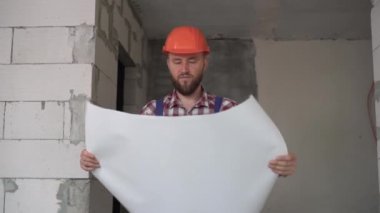 Elinde çizimleri olan bir tamirci ya da tamirci. Adam inşaat işlerini denetliyor. Foreman inşaat halinde. Şapkalı bir inşaat mühendisi. Planları olan bir inşaatçı. meslek