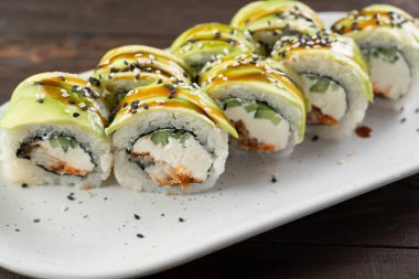 Yeşil ejderha suşi rulosu. Beyaz tabakta Japon yemeği. Somonlu suşi, krem peynir ve avokado yakın çekim. Japon restoran menüsü.