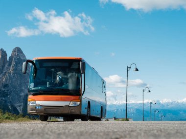 Modern orange tour bus parked in a tourist spot on a sunny day near rocky mountains. Tourism concept, logistic service.