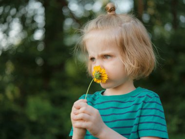 Küçük bir çocuğun yakın plan portresi. Uzun sarı saçlı ve çiçekli sarı yapraklı.