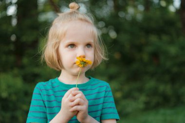 Küçük bir çocuğun yakın plan portresi. Uzun sarı saçlı ve çiçekli sarı yapraklı.
