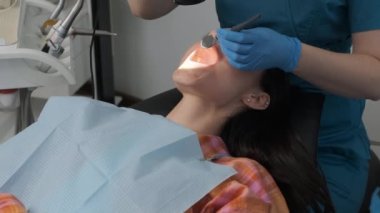 Dentist examining woman teeth and mouth with dental mirror and microscope during dental appointment.