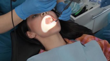 Dentist examining woman teeth and mouth with dental mirror and microscope during dental appointment.