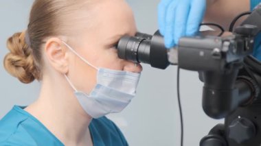The dental surgeon performs procedure looking through microscope optics. Dentist use modern stomatological equipment. 4K