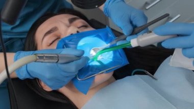 Dentist performs dental procedure on caucasian female patient with dental turbine handpiece, mirror and saliva ejector