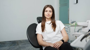 Pretty caucasian woman sitting in a chair of dental unit in dental office. Model wearing white tshirt and looking at camera